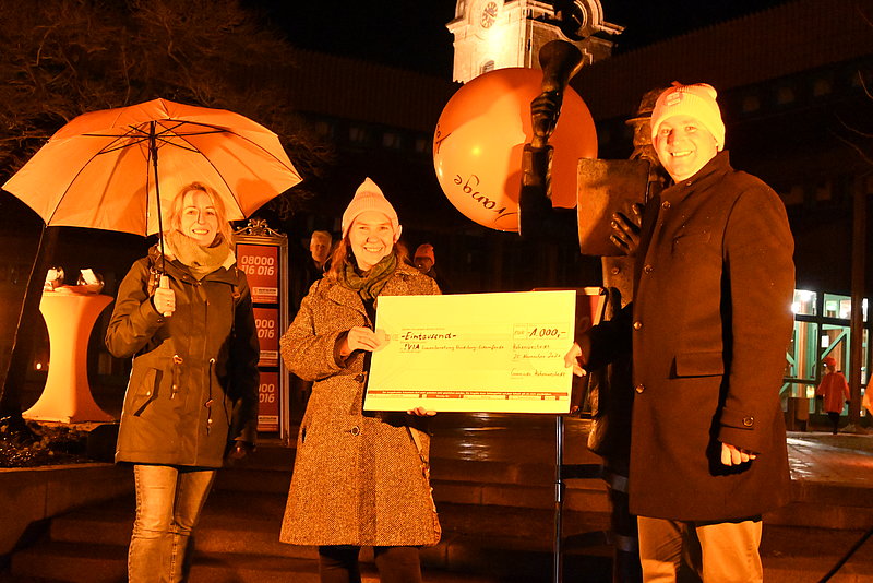 Spendenübergabe an die !VIA vor dem orange beleuchteten Rathaus am 25.11.2021